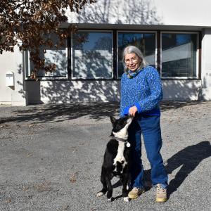 A person stands in front of the school with their dog. The dog sniffs the owner's hands.