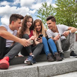 Neljä nuorta istuvat kivisillä portailla. Kaksi selaa kännykkää ja muut katsovat.