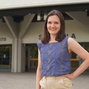 Henkilö seisoo rakennuksen edessä. Hän pitää kättään vyötäröllään.