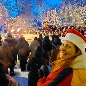 A crowd of people watching a fire show in a snowy landscape. In the foreground, a woman in an elf costume looks at the camera.
