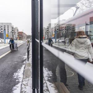 A cyclist and a bicycle trolley approach a tram stop at the same time as a tram in Hervanta.