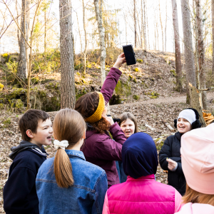 Aikuinen pitää kädellään desibelimittaria korkealla ilmassa ja lapset seuraavat tilannetta ympärillä.
