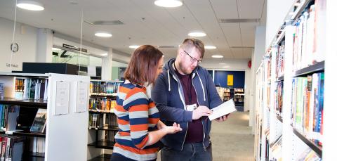 Asiakas ja virkailija katsovat yhdessä kirjaa.