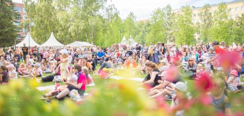 Children and adults sitting on grass at an event in summertime.