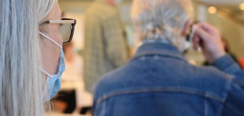 Maskia käyttävä henkilö ja puhelimessa puhuva henkilö.