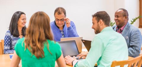 Smiling people sitting at a table with their laptops. 