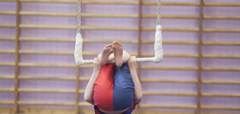 Lapsi roikkuu trapetsilla sykkyrässä, vain jalkapohjat ja kiinnipitävät kädet näkyvät.