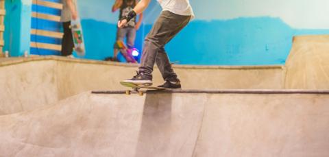 Skeittaaja skeittaa Hiedanrannan skeittihallissa. Takana kolme ihmistä katselee.  