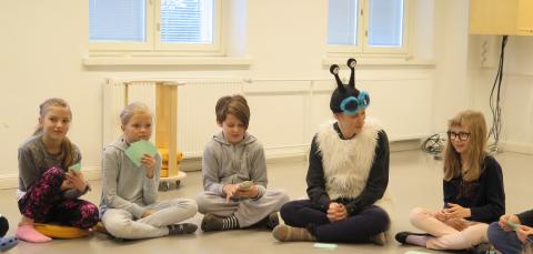 Lapsia istuu piirissä yhdessä ötökkä-roolihahmon kanssa kertomassa yhteistä tarinaa.