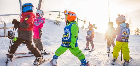 Iloisen värisiin haalareihin pukeutuneita lapsia mäessä sukset jalassa.