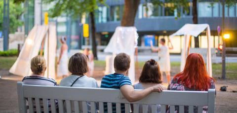 People watching a performance on a park bench.