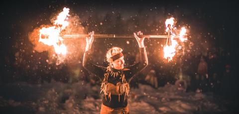 Tulitaiteilija pitää keppiä, jonka kummassakin päässä roihuaa liekit.