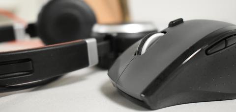 Etualalla langaton hiiri. Taustalla tietokoneen kuulokkeet.