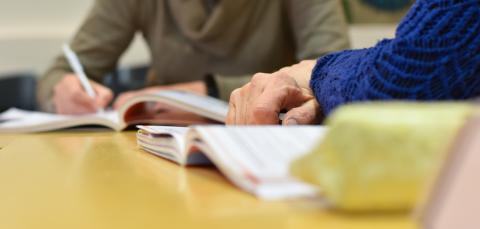 Two people are studying in front of books. One writes with a pen.