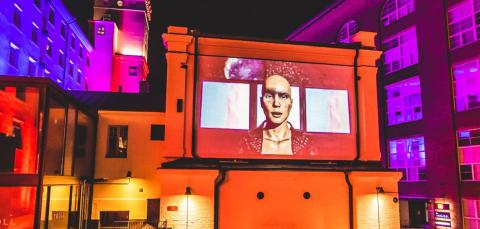 Photo from light art event, with variety of colors in the walls of the buildings, image of human being in the middle