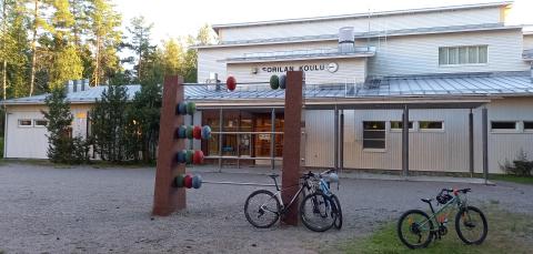Polkupyöriä Sorilan koulun pihassa. Taustalla isoja puita.