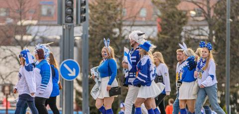 People wearing Finnish hockey fan outfits and crossing the road near Nokia Arena.