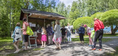 Children with their families queuing at a park meal booth. 