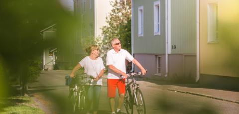 Vanhempi pariskunta taluttaa pyöriä kadulla, vieressä Pispalan puutaloja.