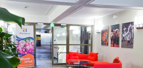 The light foyer has bright red sofas. Large photographs hang on the walls. There is also a large green plant.