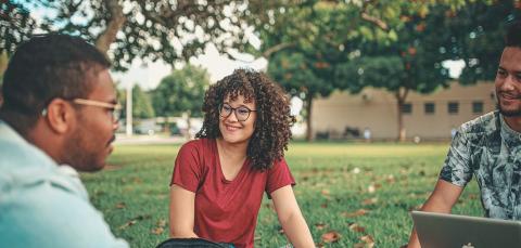 Kolme ihmistä istumassa puistossa ja keskustelemassa. 