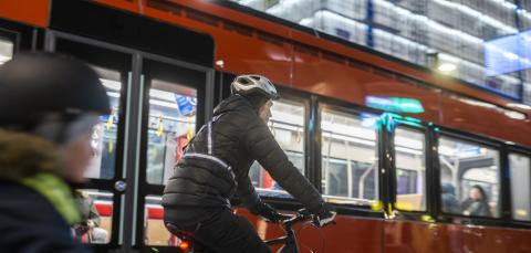 An adult and a child cycling on the street in winter. They are wearing reflectors, lights and helmets. A tram passes them. 