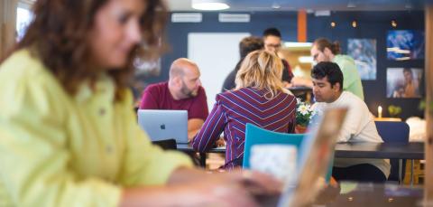 People working in a café area. In the foreground, a person with a computer.