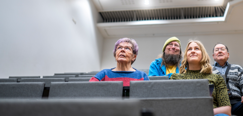 Four people are sitting side by side in the auditorium.