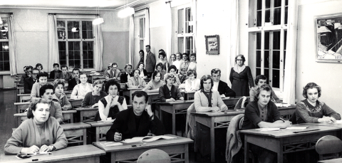 Henkilöt istuvat pulpeteissa luokkahuoneessa.