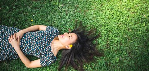 Nainen makoilee selällään nurmikolla ja hymyilee