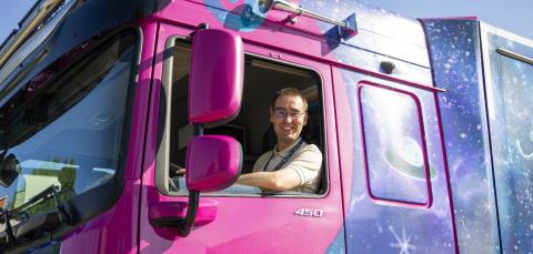 A driver looks out of a purple truck.