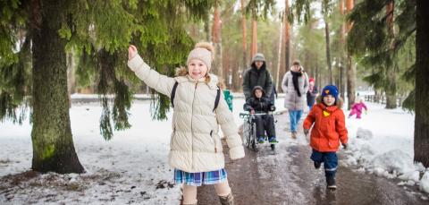 Family of six walking in a wintery forest. One of the children is grabbing a tree branch. One of the children is in a wheelchair.