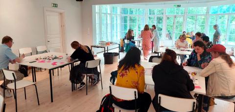 The participants are sitting at tables in the workshop and writing.