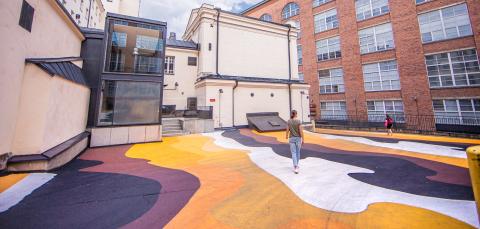 Värikäs katumaalaus Finlaysonin tiilirakennusten välissä, yksittäisiä ihmisiä kulkee alueella.