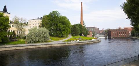 A river. In the backround pale yellow buildings on the left, a high chimney in the middle and red brick buildings on the right.