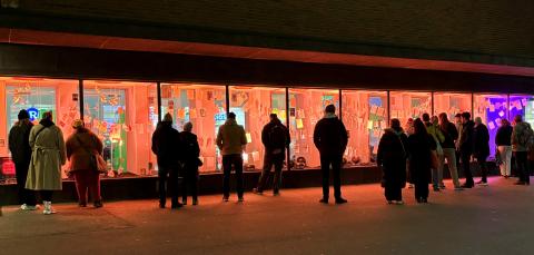 Ihmisiä tutkimassa pimeässä illassa ikkunan takana olevaa Käänne-installaatiota, jonka on toteuttanut KRIS-Tampere ry.