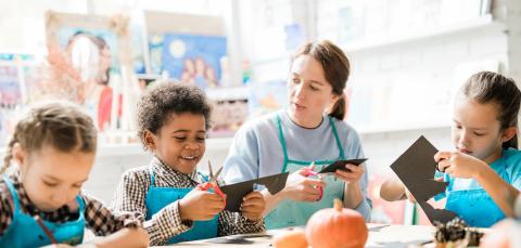 Opettaja ja kolme lasta askartelee pöydän ääressä.