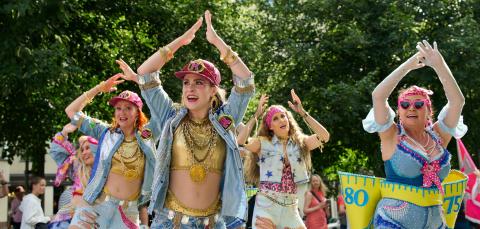 Colourfully dressed women dancing with their hands over their heads.