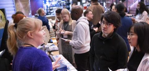 A city employee talks to two residents. Many other residents can be seen in the background.
