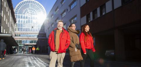 Kolme henkilöä kävelee aurinkoisena talvipäivänä Tullin alueella. Kahdella on päällään punainen ja yhdellä ruskea takki.