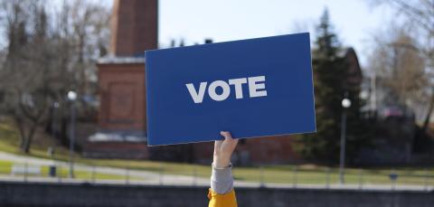 The person is holding a sign saying "vote".