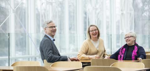 Three elderly people are sitting at a table and smiling.