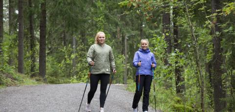 Kaksi naista sauvakävelee metsäpolulla.