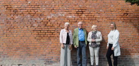 Four good-humoured seniors stand in front of a brick wall.