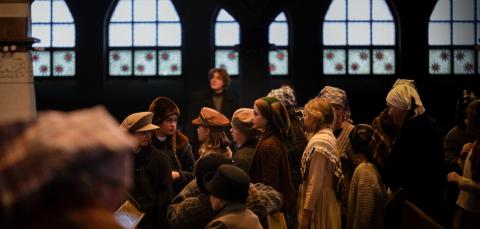 1900-luvun alun vaatteisiin puettu ihmisjoukko tuomiokirkossa, taustalla näkyvät mosaiikki-ikkunat.