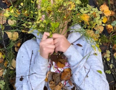 Lapsi makaa metsässä varpuja kasvojensa edessä pitäen.