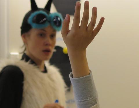 Lapsen viittaava käsi. Ötökkä-roolihahmo taustalla kuuntelee.