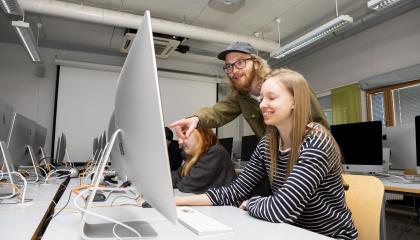 Opettaja osoittaa jotain tietokoneen näytöllä opiskelijalle.