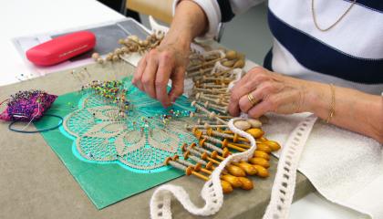 Henkilö harrastaa pitsinnypläystä. Pöydällä nypläysvälineitä.