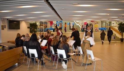 Henkilöt istuvat penkeillä soittamassa kannelta. Heidän edessään on nuottitelineitä.